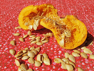Broken pumpkin in half with scattered seeds on red material.