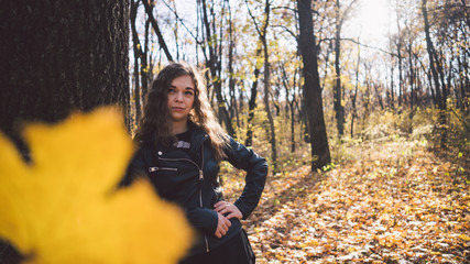 Young woman among trees. Portrait of young attractive female standing in autumn garden and looking at camera