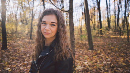 Fototapeta na wymiar Young woman among trees. Portrait of young attractive female standing in autumn garden and looking at camera