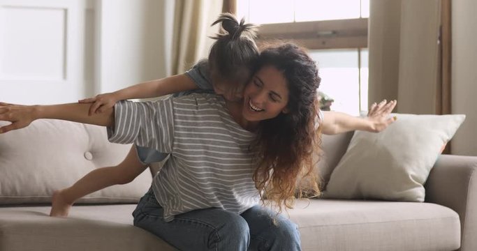 Happy mum playing piggybacking cute kid daughter sit on couch