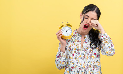 Yong woman holding a clock showing 6AM on a yellow background