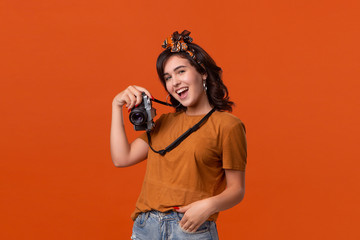 Obraz premium Pretty brunette woman making photo with a retro film camera standing isolated on an orange background.