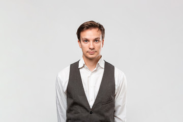 Fototapeta premium Confindent handsome man in a white shirt and grey vest looking at the camera standing isolated over grey background.