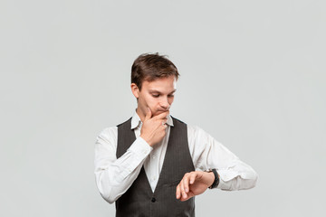 Young businessman in a white shirt and grey vest checking time on his wrist watch. Concept of...