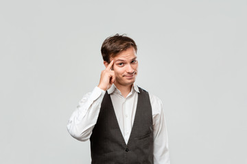 Fototapeta premium Young businessman in a white shirt and grey vest expressing gesture of shinking holding finger close to his head.