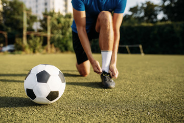 Male soccer player ties his shoelaces on boots