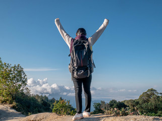 Young woman traveler raise arms to show success at peak of mountains on summer vacations day. Lifestyle hiking concept.