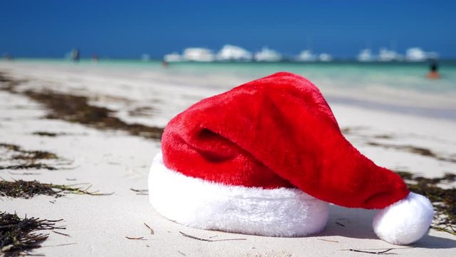 Christmas Santa Claus hat on tropical sandy shore with calm waves. Winter holidays. New Year celebration on caribbean island
