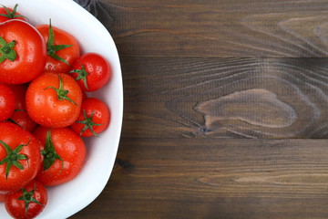 red tomatoes with green tails of different sizes and water drops in a dish on a dark wooden surface with copy space