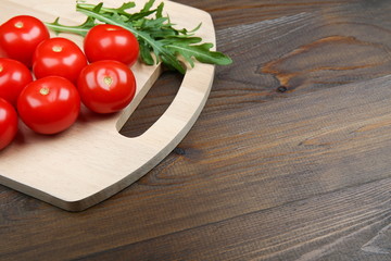 red tomatoes and arugula leaves on a cutting board on a wooden surface with copy space