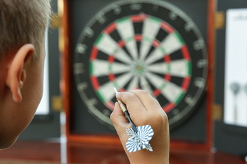 child's hand holds a dart on the background of the dartboard