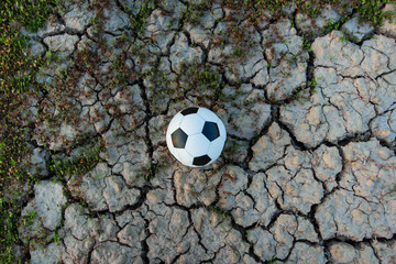 The football ball in a field that is dry and cracked in the evening sun