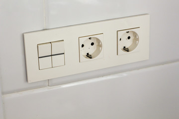 Two white socket and switch on the wall with tiles in the hotel bathroom with white tiles  on the wall. Bathroom luxury interior 