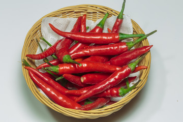Pods of hot red chili pepper in a straw basket.