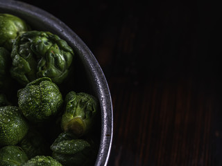 many small heads of Brussels sprouts in drops of water in a closeup lies in an aluminum drushlak pan with a handle.