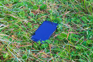 A broken smartphone lies in the grass. The touch screen is broken.