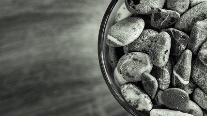 Small sea stones in a glass vessel. The idea of decorating the house with small rocks in a jar on a wooden blurred background.