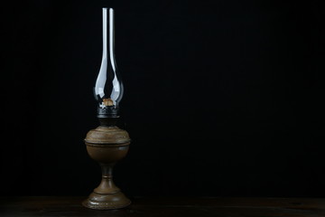 antique kerosene lamp on wooden surface on black background