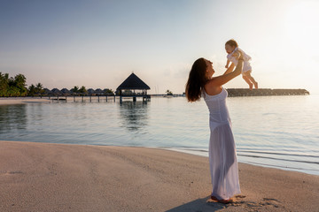 Glückliche Mutter spielt mit ihrem kleinen Baby am tropischen Strand der Malediven bei...