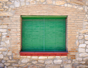 Closed window with wooden green shutters and a red windowsill in the old stone wall of the house