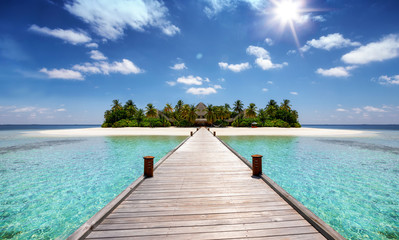 Tropisches Reisekonzept: Holzsteg führt auf eine tropische Insel mit türkisem Ozean, Kokosnusspalmen und feinem Sandstrand, Malediven