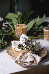 Christmas or New year table setting with empty ceramic plates, napkins, Christmas thuja wreath and burning candles on white tablecloth. Holiday mood