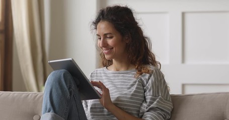 Happy young woman relaxing at home on sofa using tablet - Powered by Adobe