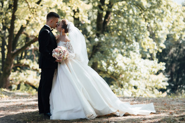 Stylish bride and groom gently kissing. Beautiful bride with modern bouquet embracing with stylish...