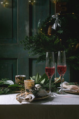 Christmas or New year table setting with two glasses red sparkling wine, plates, napkins, Christmas thuja wreath, luminous garland and burning candles on white tablecloth. Holiday mood