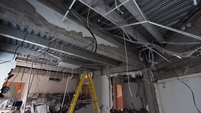 Sliding view of spacious room under construction and ceiling with wires hanging from it. Demolition work in apartment
