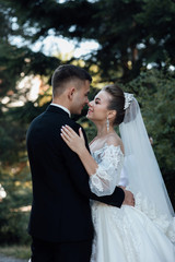 Stylish bride and groom gently kissing. Beautiful bride with modern bouquet embracing with stylish groom in summer park. Sensual romantic moment.  Wedding. Stylish and beautiful.