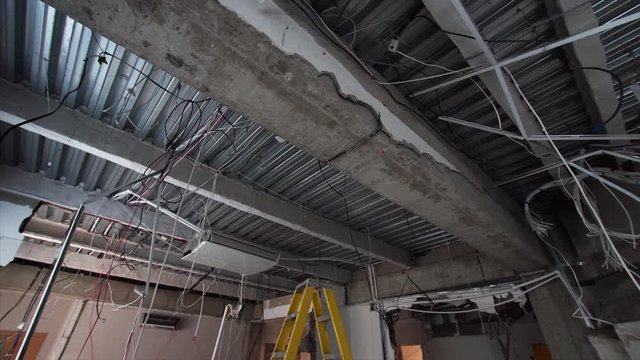 Spacious room under construction and ceiling with wires hanging from it. Demolition work in apartment