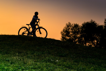 Silhouette boy riding bicycle at sunset or sunrise background