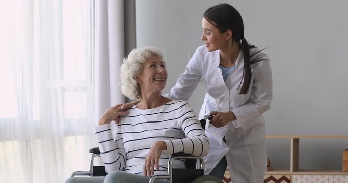 Young woman nurse caregiver talk help senior grandmother on wheelchair