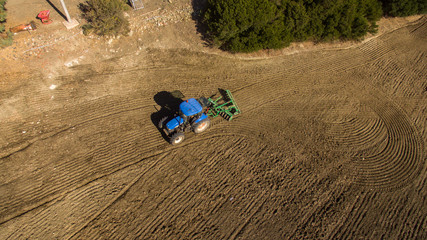 aerial view of blue tractor in operation crushing the ground after sowing