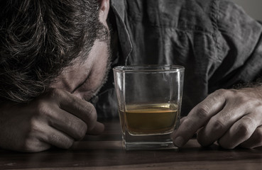 depressed and thoughtful alcoholic man on his 40s in front of whiskey glass wasted and stressed holding on temptation to drink in alcohol addiction and alcoholism problem