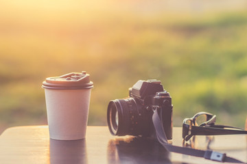 Coffee mugs white plastic and classic camera models on a wooden table against sunlight and a blurred background.