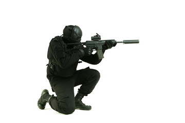 a man in a black military uniform and mask of cyborg shoots machine gun sitting on his knee on white background with copy space