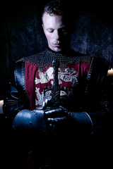 Portrait of handsome medieval knight in suit of armour with beard looking down in contemplation