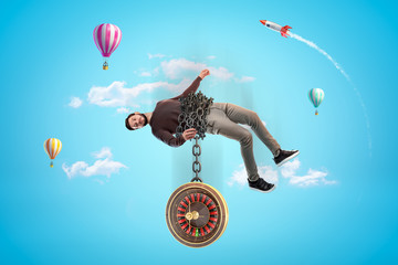 Man in casual clothes chained to roulette with hot air balloons and silver red space rocket in the air on blue background
