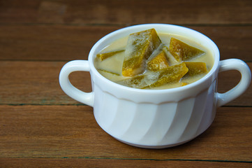 Pumpkin in sweet coconut milk in white bowl, popular Thai dessert on wooden background