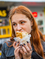 portrait of young teenager redhead girl with long hair eating chicken shawarma on street