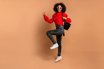 Full body portrait of excited young black woman jumping with joy over beige background.Full length portrait of a cheerful young african woman celebrating success while jumping isolated. Copy space.