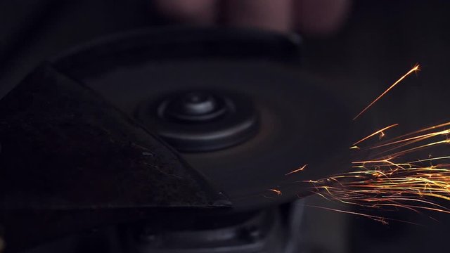 Man sharpening axe with grinder in the dark with sparks. Slow motion