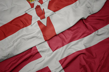 waving colorful flag of denmark and national flag of northern ireland.