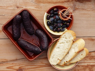 Morcilla/Baldana on a ceramic plate with bread and olives on a wooden table. (Top view)