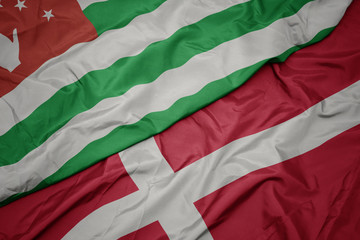 waving colorful flag of denmark and national flag of abkhazia.