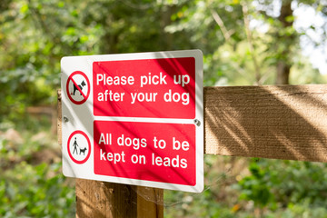 Shallow focus of two warning signs for dog owners located at the entrance to a country park and lake area. Recently added due to dogs being allowed to foul