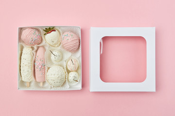 Open gift box with fruits covered in white and pink chocolate are on the pink background