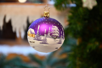 Blue christmas ball. Purple and white Christmas ornament closeup with blurry background. Beautiful Christmas ball with hand painted farmhouse in winter rural landscape. Winter holiday decor. Tradition